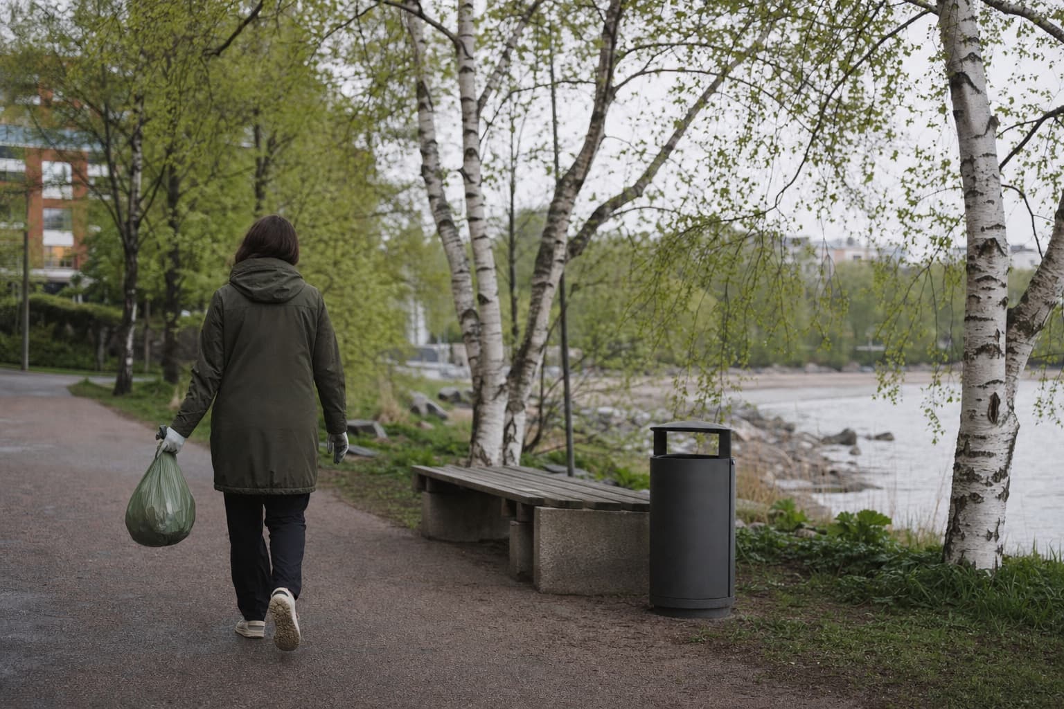 Helsinkiläisen puistoreitin varrella näkyy roskis, penkki ja siisti kulkuväylä pehmeässä kevätvalossa.